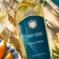 Fles Tornicola Pinot Grigio met glas witte wijn en zomerse borrelplank in zonnige mediterrane sfeer.